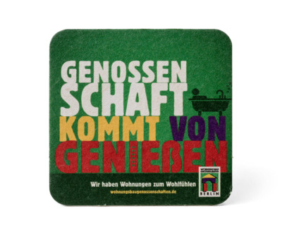 Quadratischer Bierdeckel aus Pappe mit abgerundeten Ecken. Die bunte Aufschrift auf grünem Hintergrund lautet: Genossenschaft kommt von genießen. In der rechten unteren Ecke ist das Logo der Wohnungsbaugenossenschaften Berlin.
