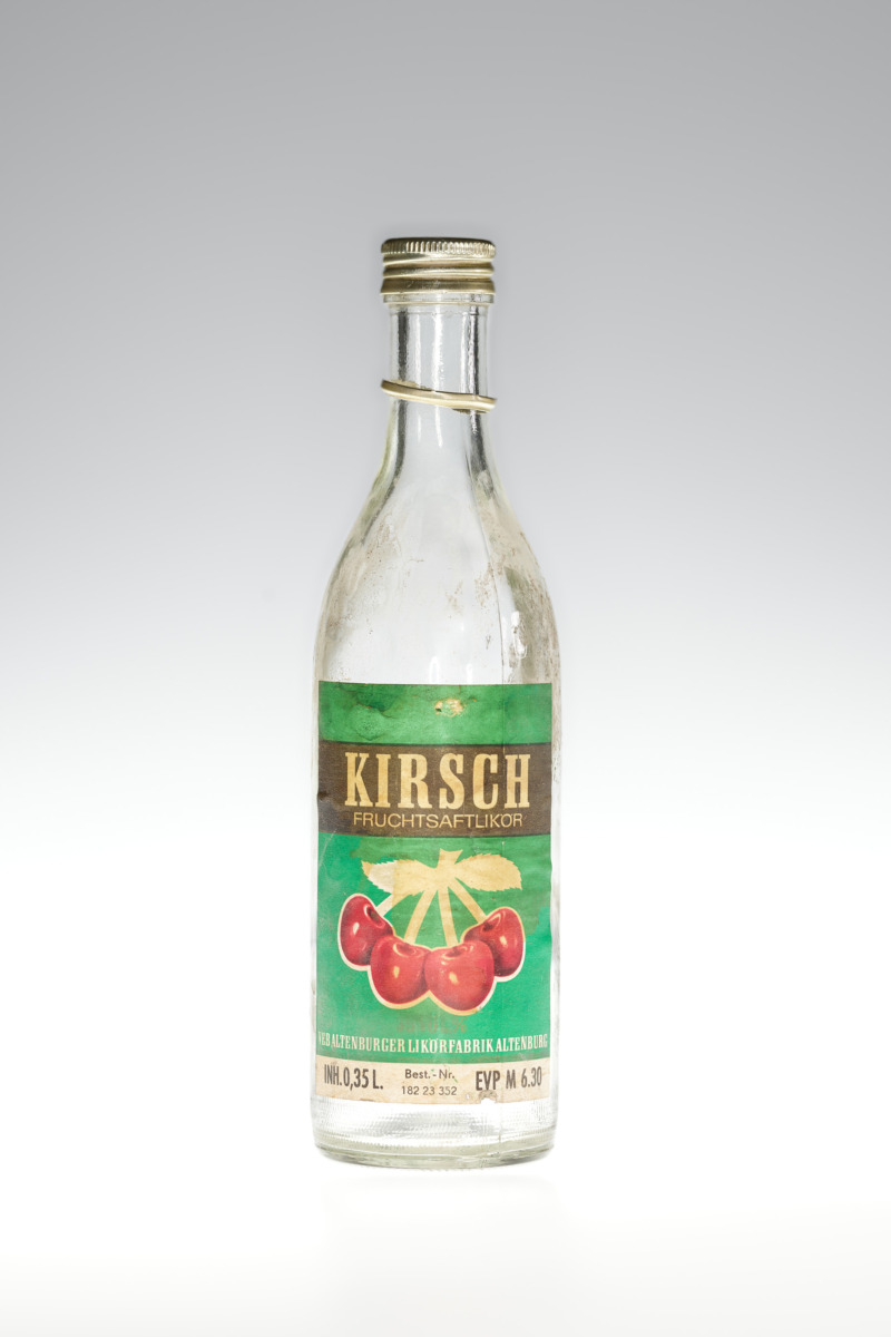 Kleine leere Kirschflasche mit grünen Etikett und vier Kirschen