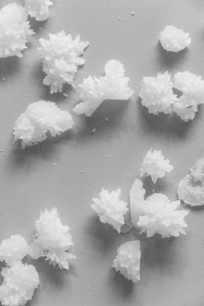 Kleine Häufchen weißen Pulvers, das wie gefrorener Schnee aussieht auf grauem, synthetischem Hintergrund.
