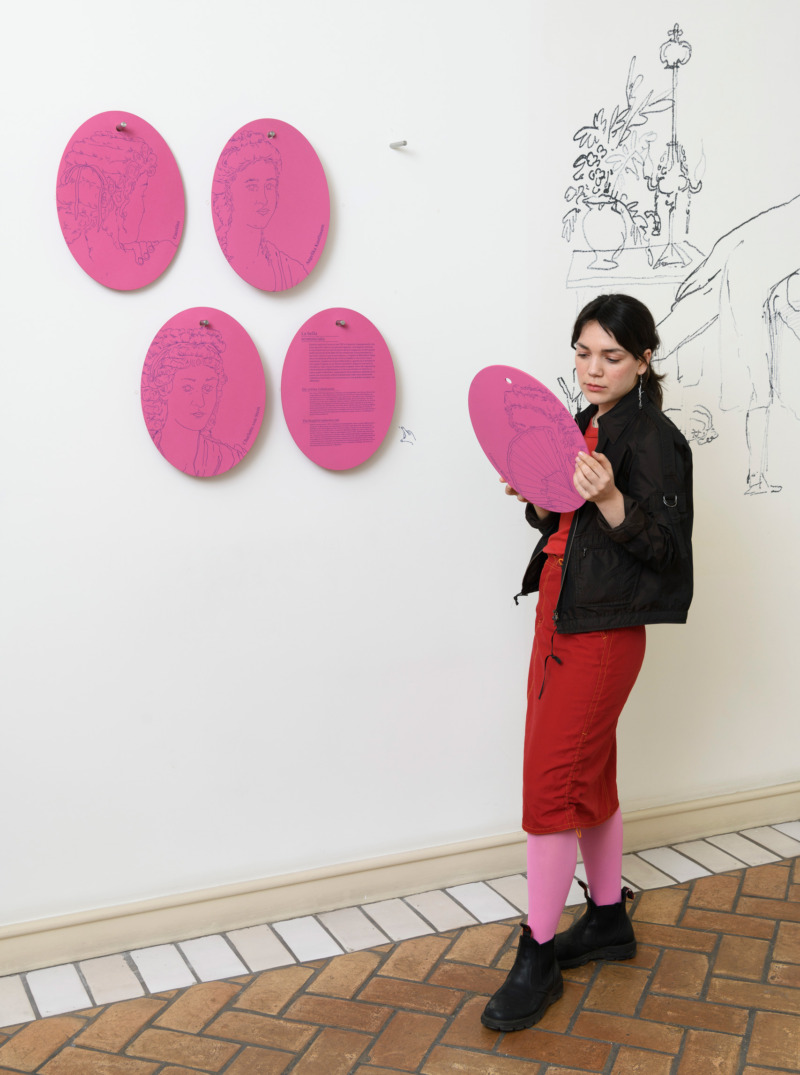 Junge Frau hält runde pinke Karten in einem Ausstellungsraum.