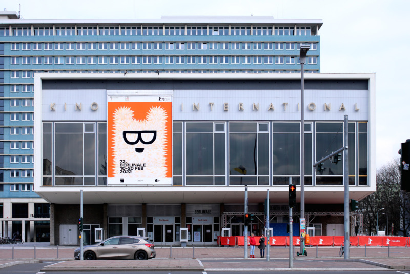 Außenansicht des Kino International in Berlin mit einem großen orange-weißen Berlinale-Plakat, das einen Bären mit Brille zeigt