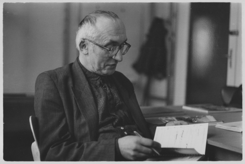 Schwarz-Weiß-Fotografie von Heinz Hirdina, der an einem Tisch sitzt und aufmerksam in einem aufgeschlagenen Notizbuch blättert oder schreibt